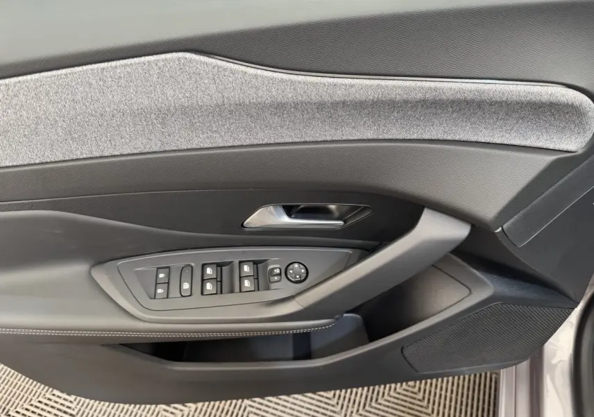 Vue rapprochée de la porte avant gauche de la Peugeot 308 gris clair, avec commandes électriques et habillage tissu gris.