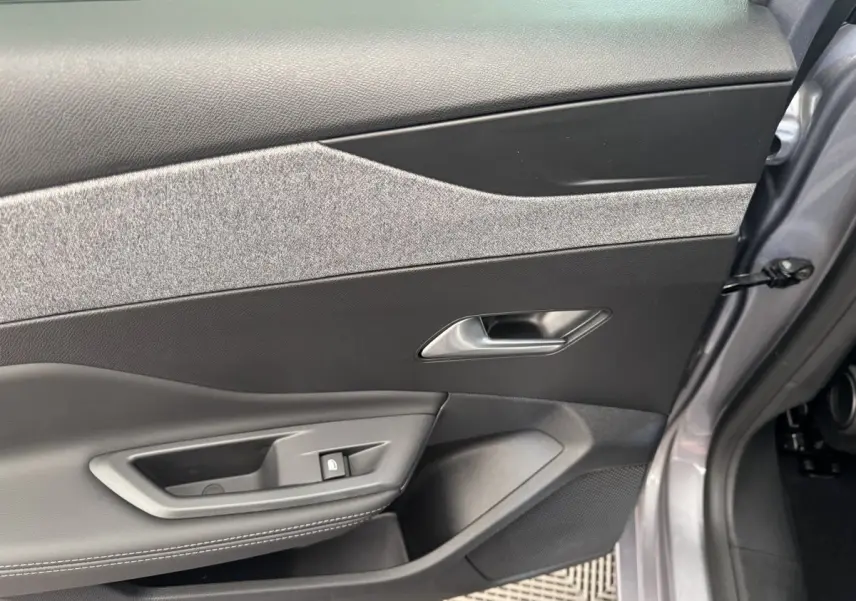 Vue intérieure côté gauche de la porte avant gris clair de la Peugeot 308 2026 avec garniture tissu et commandes électriques.