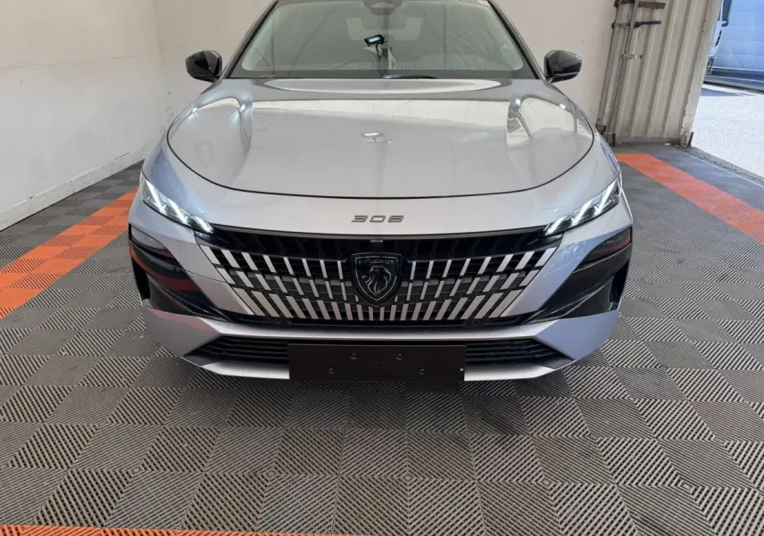 Vue frontale d'une Peugeot 308 gris clair 2026 avec calandre distinctive et phares LED fins allumés.