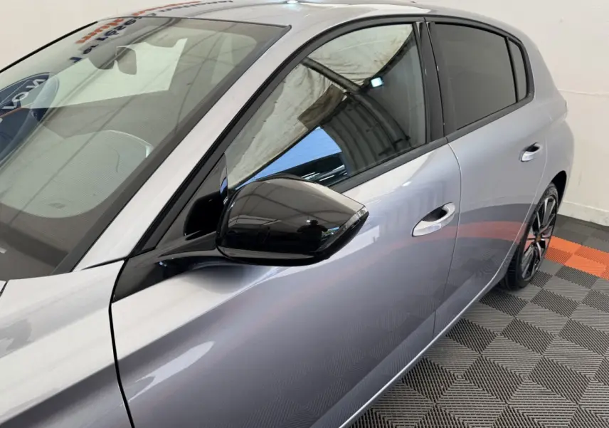 Vue latérale droite rapprochée d'une Peugeot 308 gris clair avec rétroviseur noir brillant et vitres teintées.