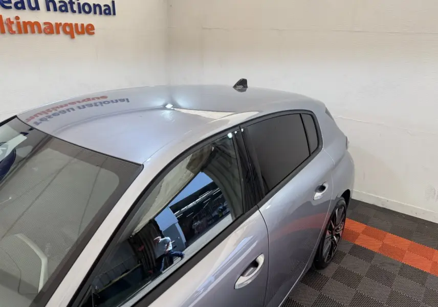 Vue 3/4 arrière droite d'une Peugeot 308 gris clair avec vitres teintées dans un showroom.