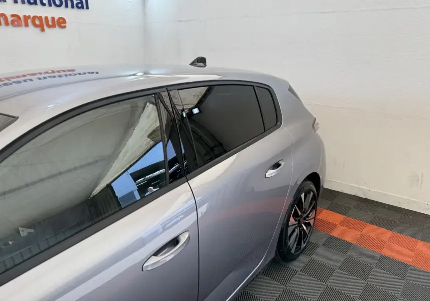 Vue 3/4 arrière côté droit d’une Peugeot 308 gris clair avec jantes alliage et vitres teintées dans un showroom.
