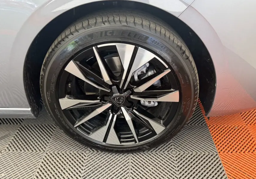Gros plan sur la roue avant droite d'une Peugeot 308 gris clair, jante alliage noire et argentée au design moderne.