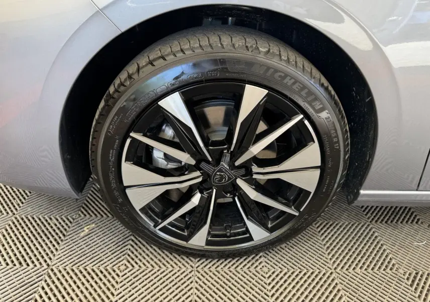 Gros plan sur la roue avant gauche de la Peugeot 308 gris clair, jante alliage noire et argentée au design moderne.