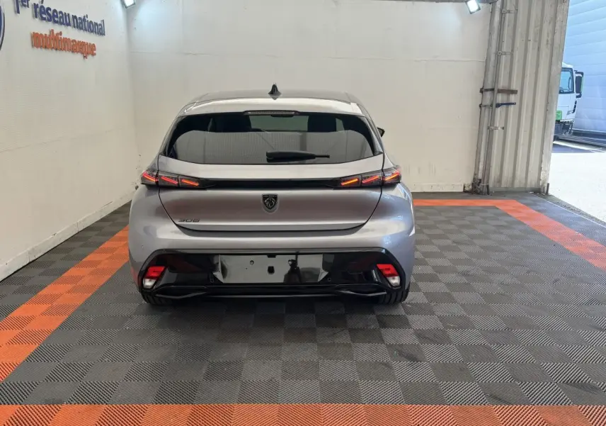 Vue arrière d'une Peugeot 308 gris clair 2026 avec feux LED et logo noir sur fond clair en intérieur showroom.