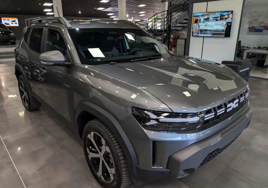 Vue 3/4 avant du Dacia Duster Hybrid-G 150 CH 4x4 gris schiste, avec calandre moderne et jantes bi-ton en showroom.