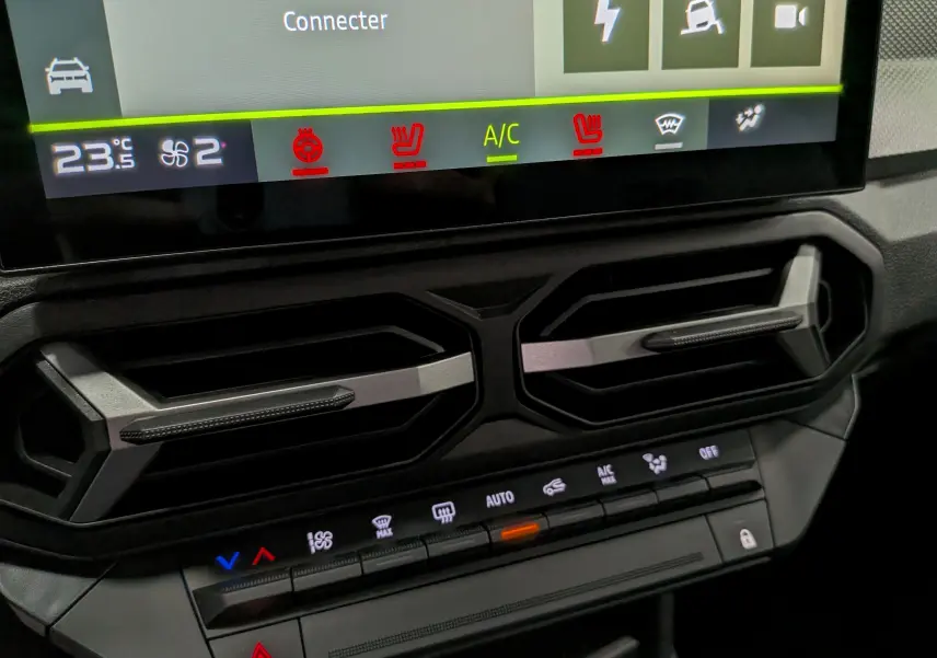 Gros plan sur la console centrale du Dacia Duster gris, montrant les aérateurs hexagonaux et les commandes de climatisation.
