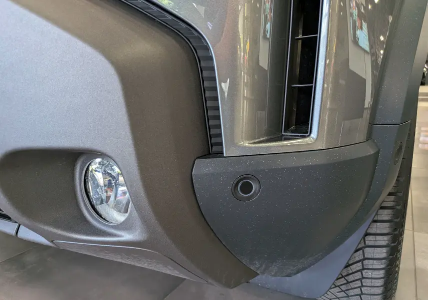 Gros plan sur le pare-chocs avant droit gris schiste du Dacia Duster Hybrid-G 150 CH 4x4 avec antibrouillard et capteur de stationnement.
