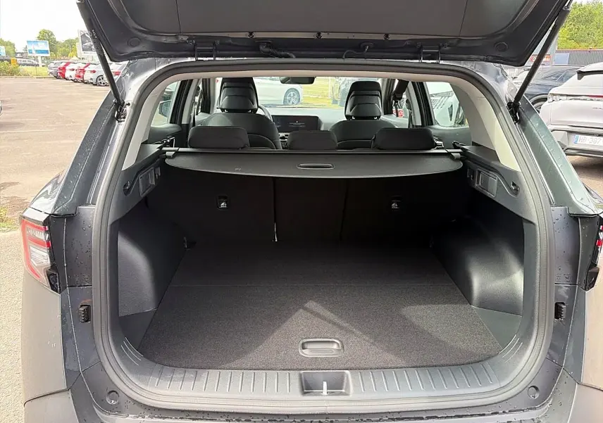 Coffre ouvert vu de l'arrière d'un KIA Sportage 1.6 hybride gris eclipse avec cache-bagages et banquette arrière visible.