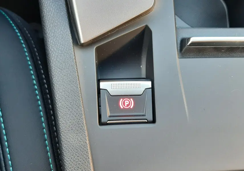 Gros plan sur le bouton de frein à main électronique rouge dans la console centrale d'une Peugeot 308 Bleu Obsession.