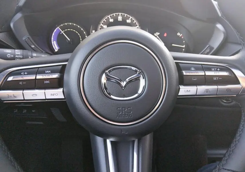 Vue rapprochée du volant noir de la Mazda MX-30 électrique 2021 avec commandes intégrées et logo central chromé.