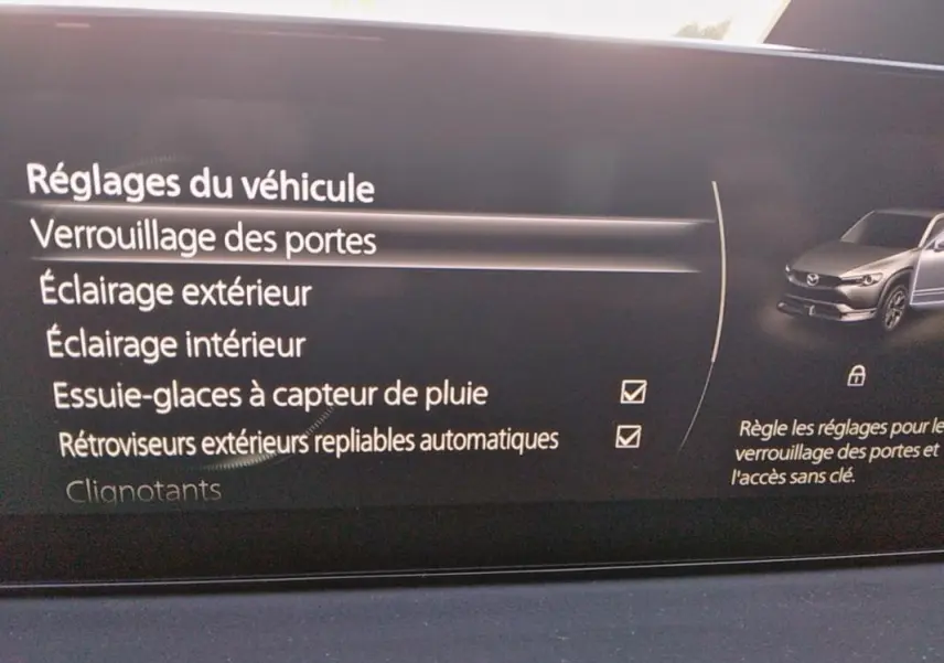 Écran intérieur du Mazda MX-30 2021 montrant les réglages de verrouillage des portes et options d'éclairage, avec illustration du véhicule gris.
