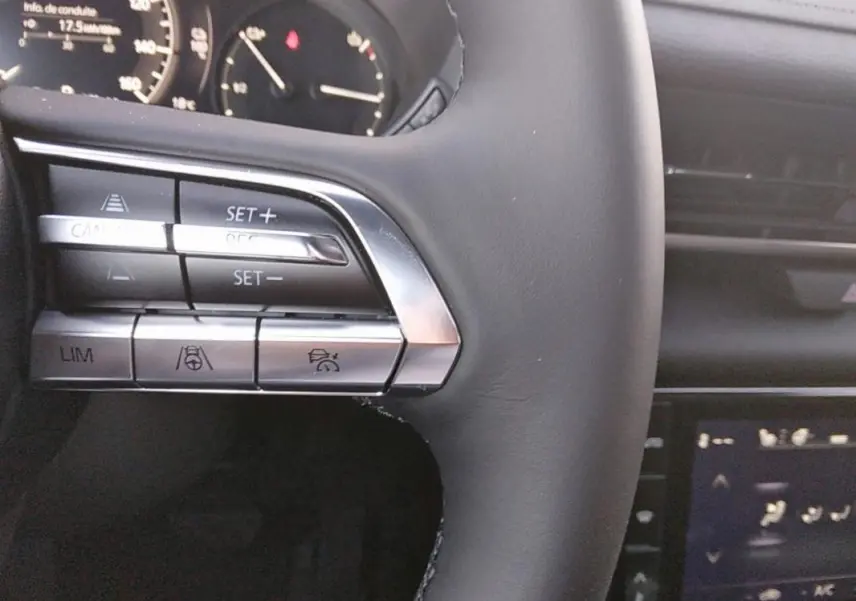 Gros plan sur les commandes au volant gris du Mazda MX-30 électrique, mettant en valeur les boutons de régulateur de vitesse.