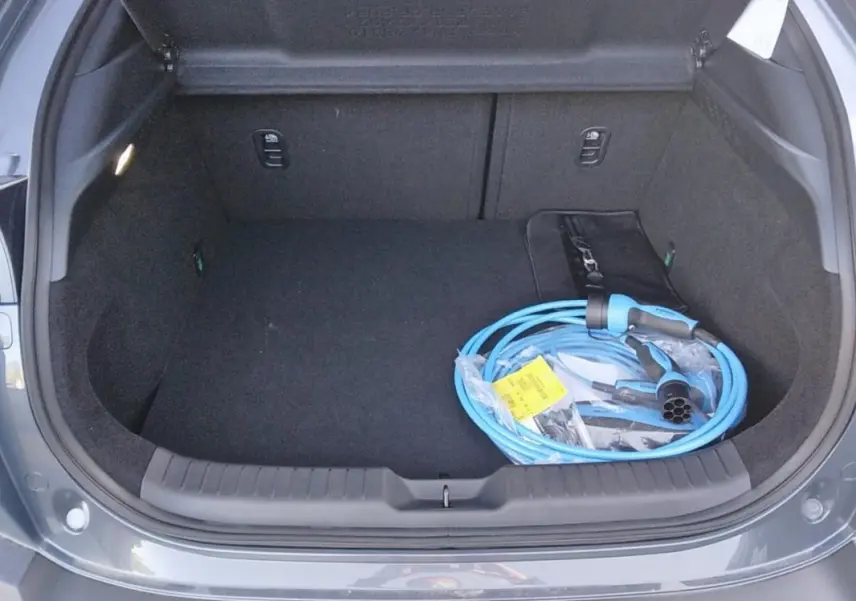 Coffre ouvert d'une Mazda MX-30 gris 2021, avec câble de recharge électrique bleu visible à l'intérieur.