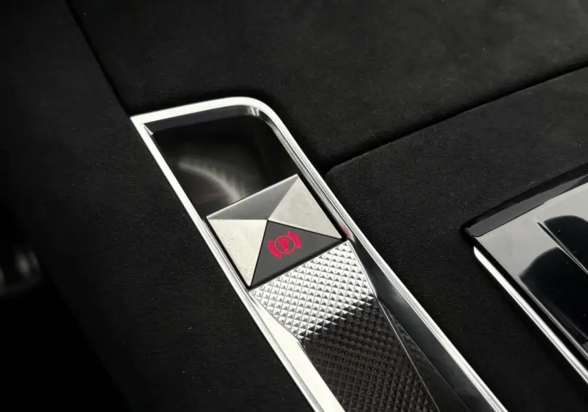 Gros plan sur le frein de stationnement électrique chromé dans la console centrale en Alcantara noir du DS7 gris laqué.