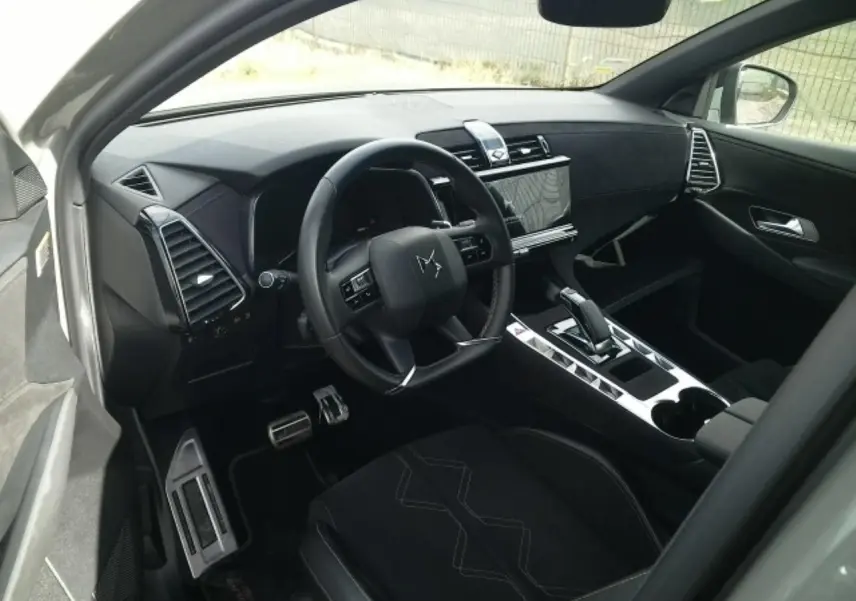 Vue intérieure côté conducteur du DS7 2024 gris laqué, mettant en valeur le volant cuir, la console centrale brillante et l'écran tactile.
