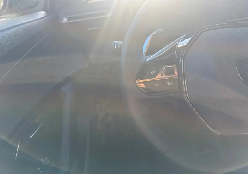 Vue partielle de l’intérieur du Peugeot 2008 Hybrid gris, avec le volant multifonction et commandes au volant visibles.