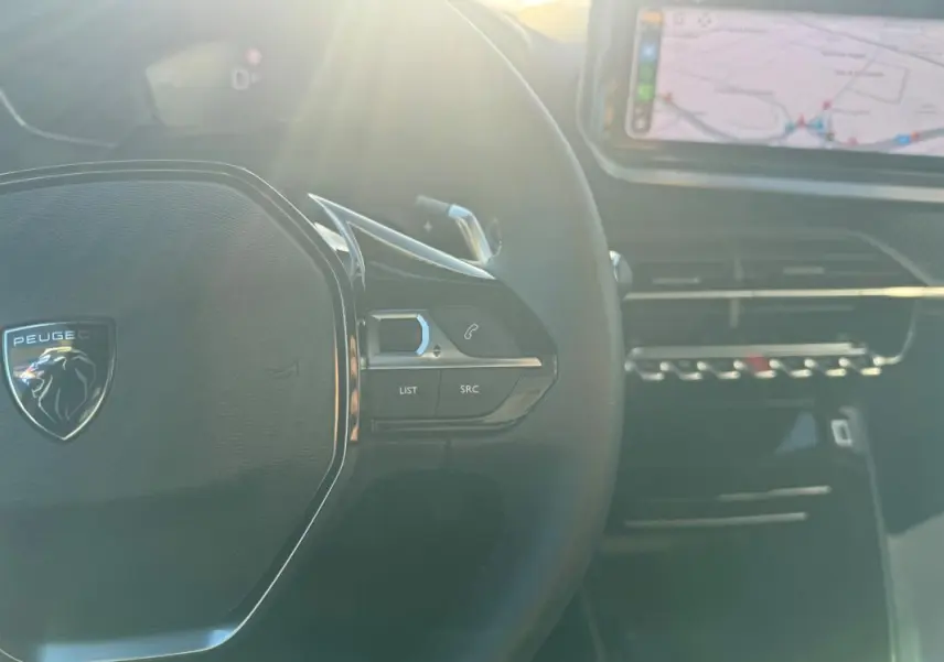Vue rapprochée du volant noir du Peugeot 2008 Hybrid 136 gris avec commandes et écran tactile en arrière-plan.