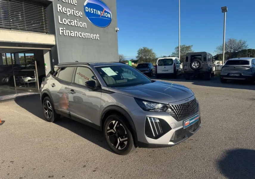 Peugeot 2008 Hybrid gris en 3/4 avant droit, avec barres de toit et jantes alliage 17 pouces, stationnée devant un concessionnaire.