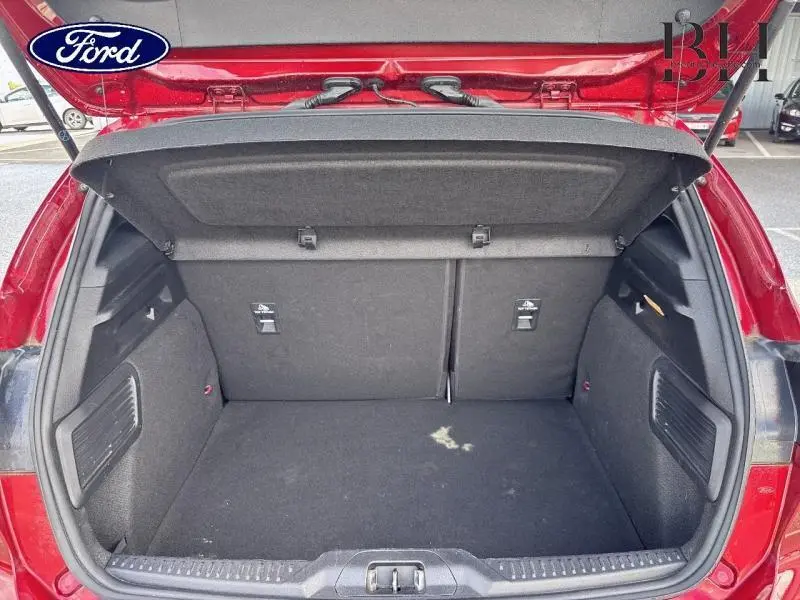 Coffre ouvert vu de l'arrière d'une Ford Focus 1.0 EcoBoost rouge, montrant un espace de chargement propre et spacieux.