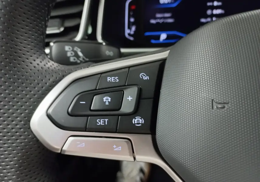 Gros plan sur les commandes de régulateur de vitesse au volant perforé du Volkswagen T-Roc 2025, finition R-Line.