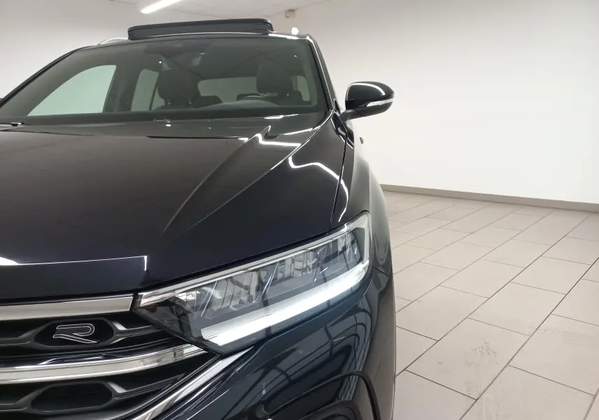 Vue avant droite du Volkswagen T-Roc noir intense avec projecteur LED allumé et toit ouvrant partiellement visible.