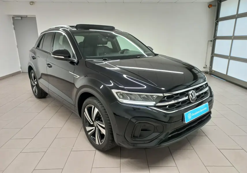 Vue 3/4 avant d’un Volkswagen T-Roc noir intense 2025 avec toit ouvrant panoramique et jantes R-Line distinctives.