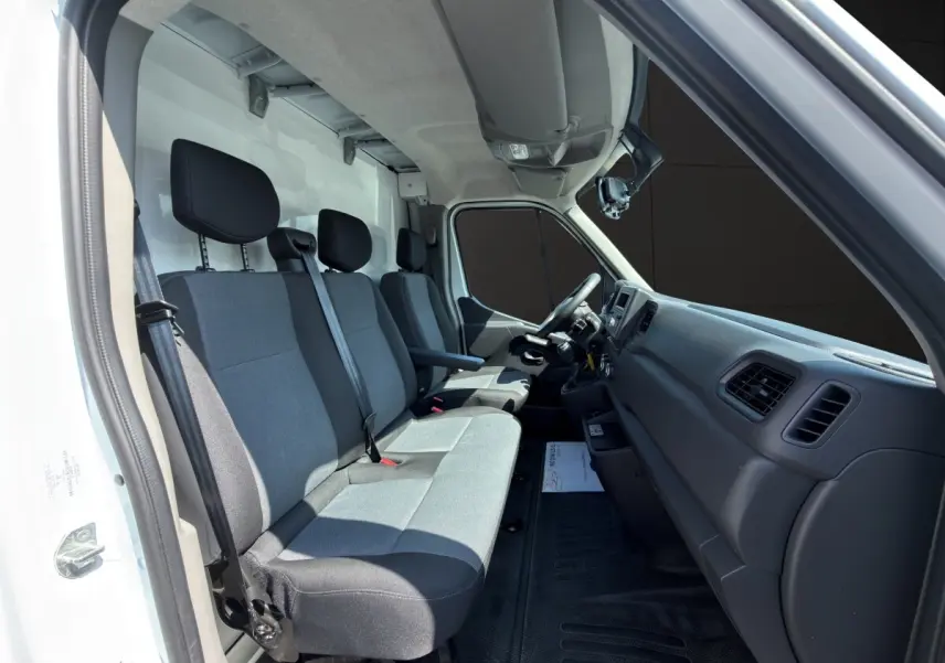 Vue intérieure côté conducteur du Renault Master 2024 blanc, montrant les sièges avant gris et le tableau de bord noir.