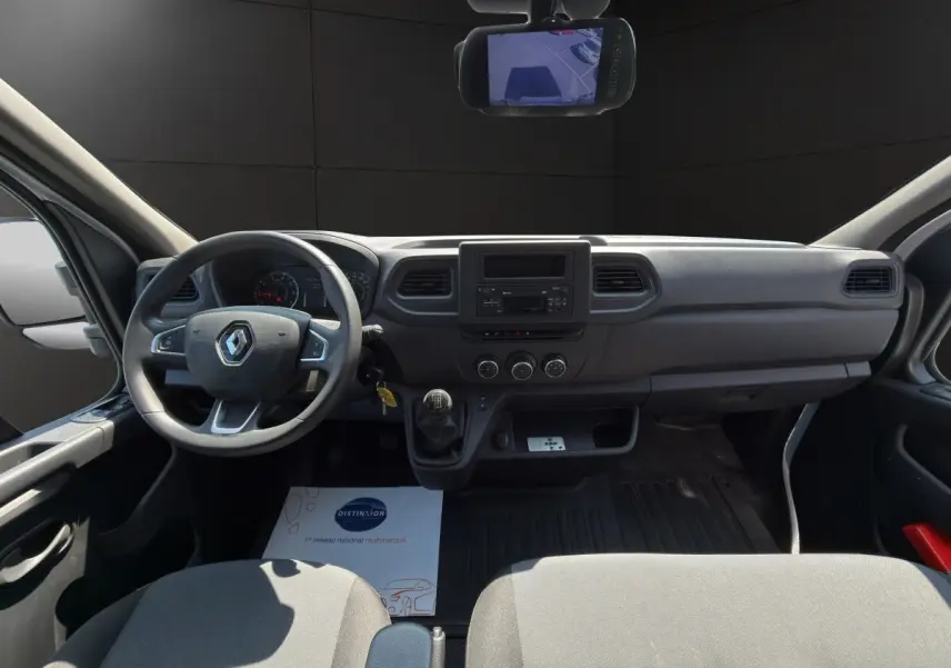 Vue intérieure avant du Renault Master 2024, tableau de bord gris avec volant, boîte manuelle et écran de rétrovision.