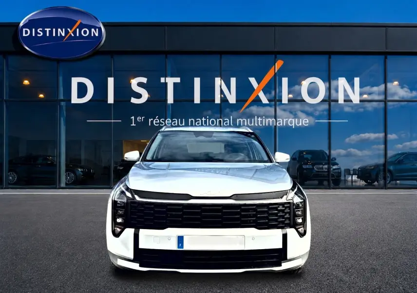 Vue frontale d'un KIA SPORTAGE 1.6 hybride blanc avec calandre noire et phares LED, devant une vitrine Distinxion.