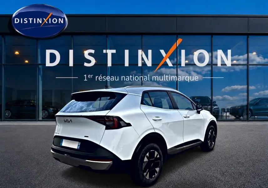 KIA SPORTAGE 1.6 hybride blanc en 3/4 arrière droit, avec jantes alu noires et feux arrière LED distinctifs.