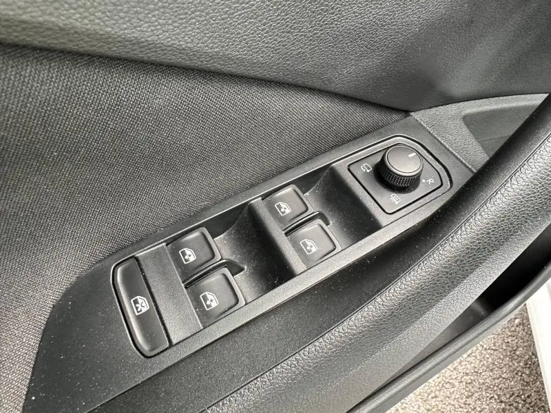 Gros plan sur les commandes de lève-vitres et rétroviseurs côté conducteur de la Skoda Scala blanc cristal 2025.