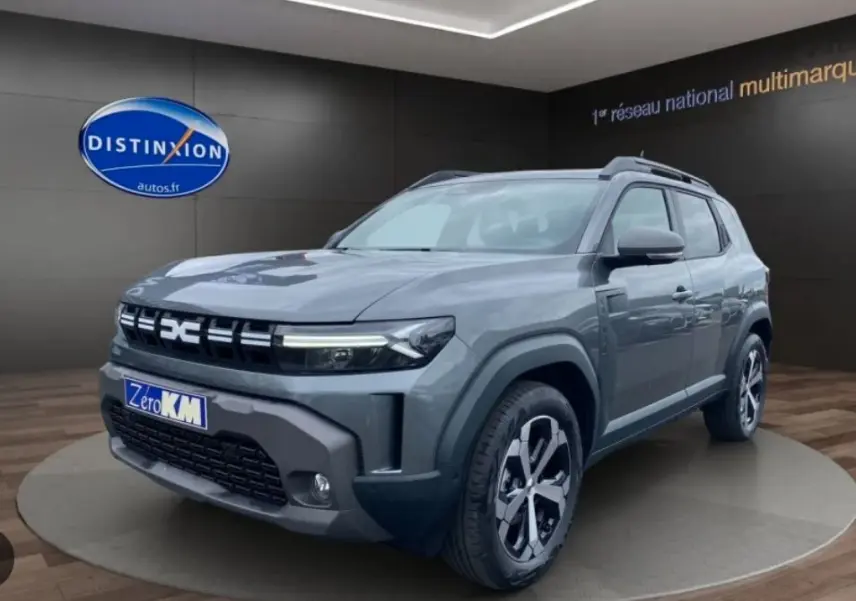 Vue 3/4 avant droit du Dacia Duster 1.8 Hybrid 155 Journey en gris schiste métallisé avec jantes bi-ton et calandre distinctive.