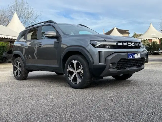 Dacia Duster 1.8 Hybrid 155 gris schiste en 3/4 avant droit, avec jantes bi-ton et calandre marquée DC.