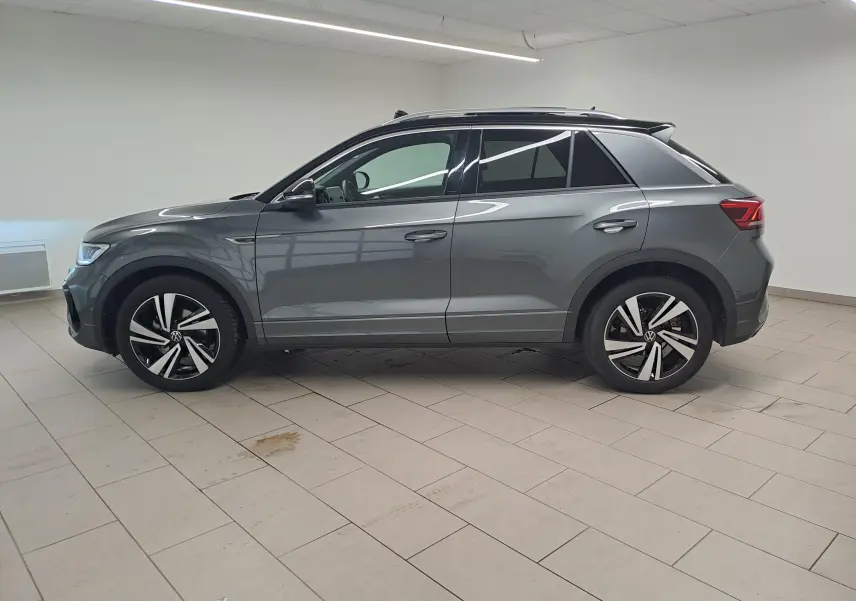 Vue de profil côté gauche d'un Volkswagen T-Roc 2025 gris Indium avec toit noir et jantes R-Line.