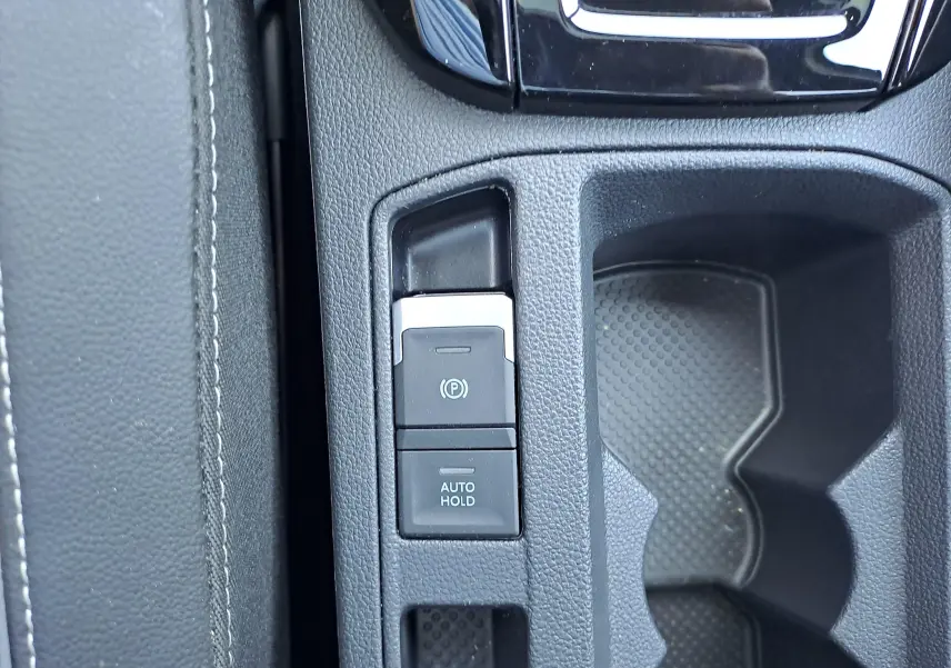 Gros plan sur la console centrale du Volkswagen T-Roc 2025, boutons de frein à main électrique et auto hold visibles.