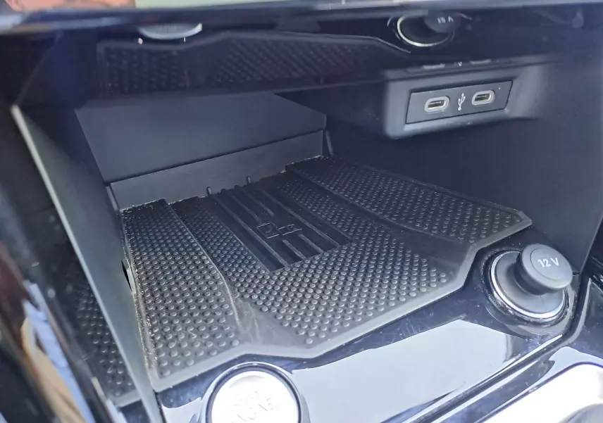 Gros plan sur la console centrale du Volkswagen T-Roc 2025, avec prise 12V, ports USB-C et tapis antidérapant noir.