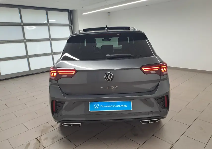 Vue arrière d'un Volkswagen T-Roc gris Indium avec toit noir et feux LED allumés dans un garage.