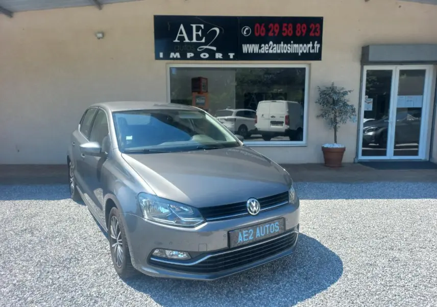 Volkswagen Polo gris vue 3/4 avant droit, avec calandre noire et jantes alliage, stationnée devant un commerce.