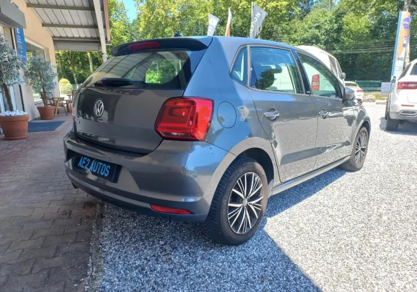 Volkswagen Polo gris vue 3/4 arrière droit, avec jantes alliage et feux arrière distinctifs, stationnée sur gravier.