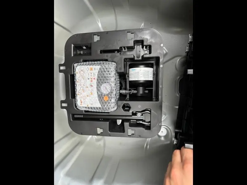Vue en plongée sur le coffre d'une Renault Clio 2025 gris, montrant le kit de réparation pneu rangé dans le compartiment.