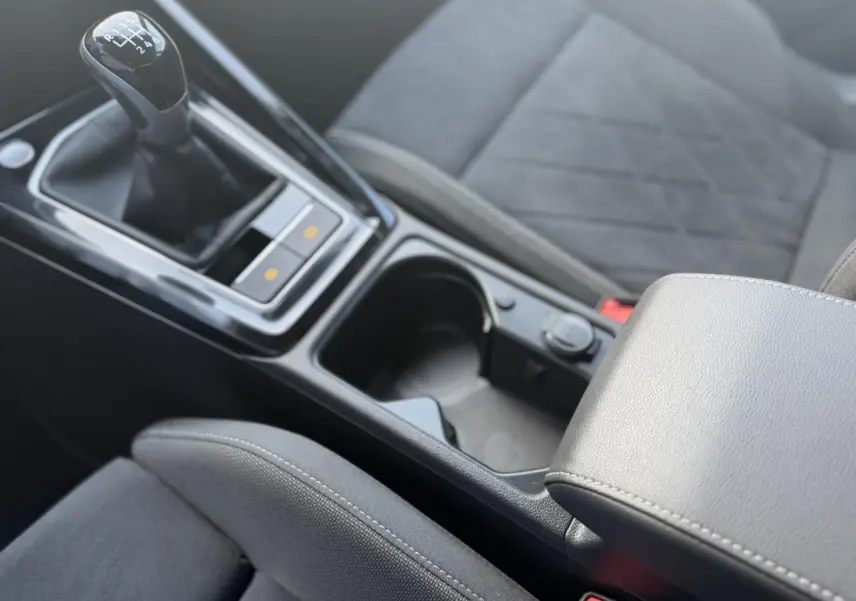Gros plan intérieur sur la console centrale et levier de vitesses manuel de la Volkswagen Golf VIII 1.5 TSI noir avec accoudoir réglable.