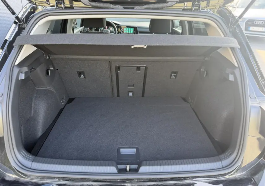 Coffre ouvert vu de l'arrière d'une Volkswagen Golf VIII noire, montrant un espace de chargement propre et spacieux.