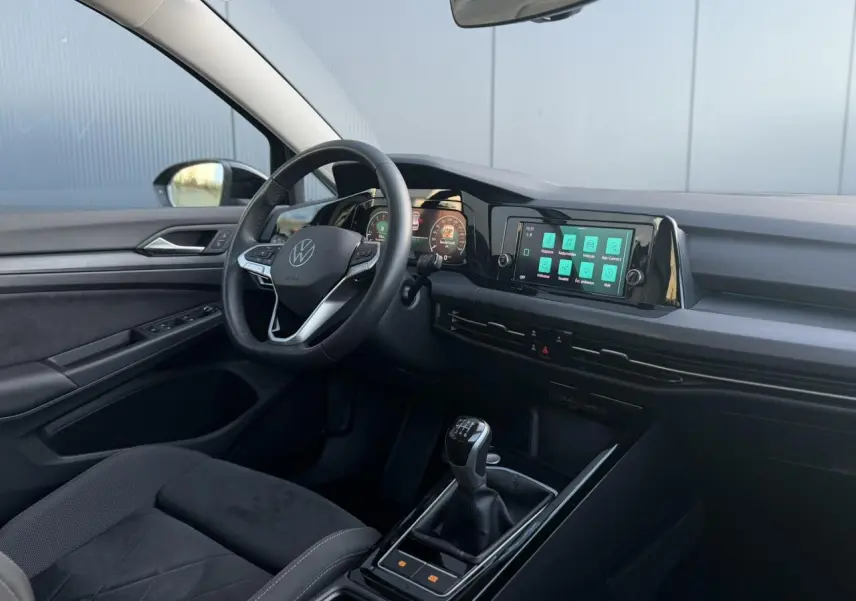 Intérieur de la Volkswagen Golf VIII 2024, vue côté conducteur, tableau de bord numérique et levier de vitesses manuel noir.