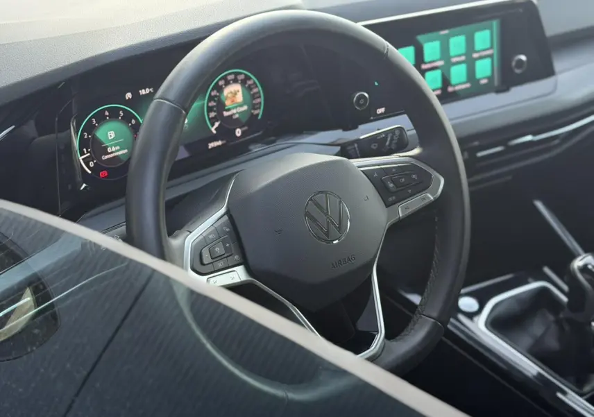 Vue intérieure centrée sur le volant multifonction noir et le tableau de bord digital lumineux d'une Volkswagen Golf VIII 2024.