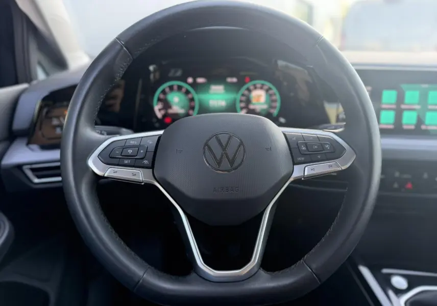 Volant multifonction noir de Volkswagen Golf VIII 2024 avec tableau de bord numérique et écran tactile en arrière-plan.