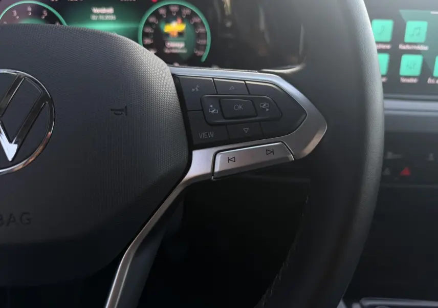 Gros plan sur le volant multifonction noir de la Volkswagen Golf VIII 2024 avec commandes et tableau de bord numérique en arrière-plan.