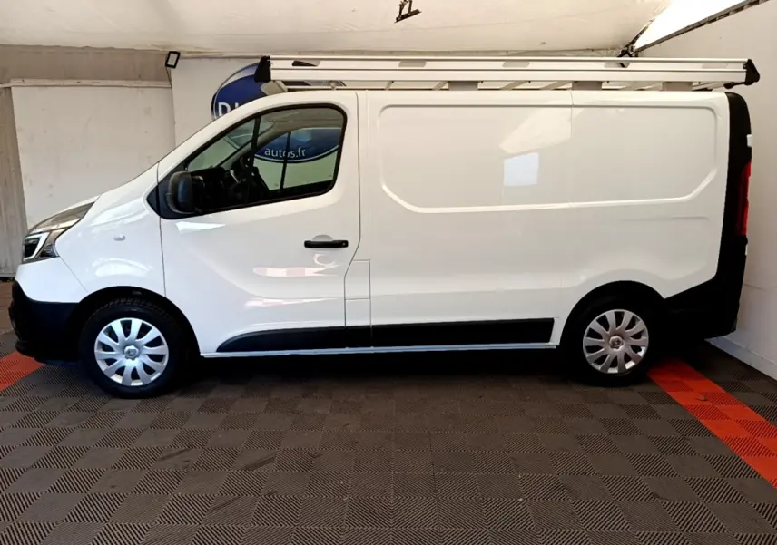 Profil latéral droit d’un Renault Trafic Fourgon blanc 2021 avec galerie de toit et jantes tôles argentées.