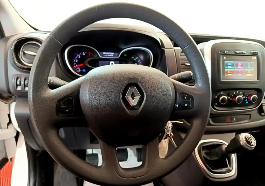 Vue intérieure centrée sur le volant noir Renault du Trafic Fourgon blanc avec tableau de bord et levier de vitesses manuel.