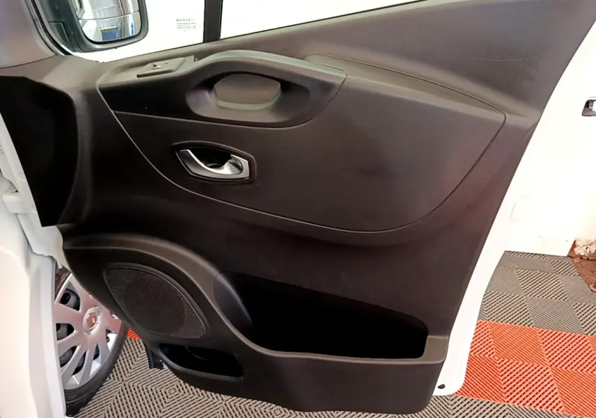 Vue rapprochée de la porte avant gauche noire du Renault Trafic Fourgon blanc, avec poignée et haut-parleur intégrés.